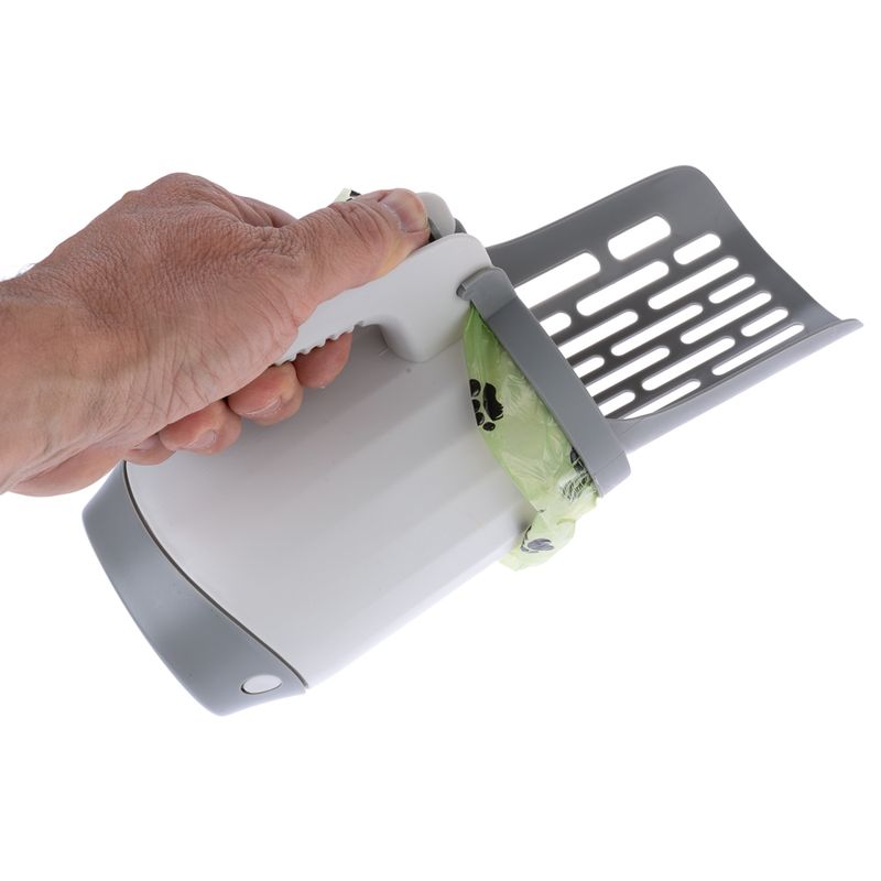 Hand holding grey scoop with integrated container and attached green bag with paw pattern, suitable for cleaning pet litter.