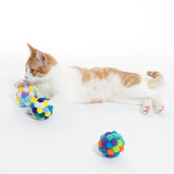Cat playing with colourful, padded fabric balls. Three coloured play balls visible: yellow-blue, pink-purple and green-orange.