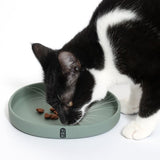 Black and white cat eating from a green food bowl with Tiaki logo. Some brown food pieces are visible in the bowl.
