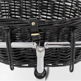Close-up of a black basket made of woven material with metal holder and leather strap with gold buckle.