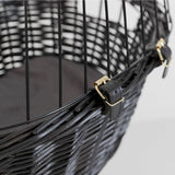 Close-up of a black wicker basket with metal mesh and leather strap with gold-coloured buckles.