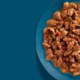 Close-up of wet food in gravy with pieces of meat and small vegetable chunks in a blue bowl.