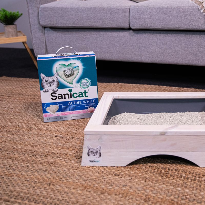 Sanicat Active White cat litter with lotus blossom scent, packaging next to a filled litter tray on a carpet.