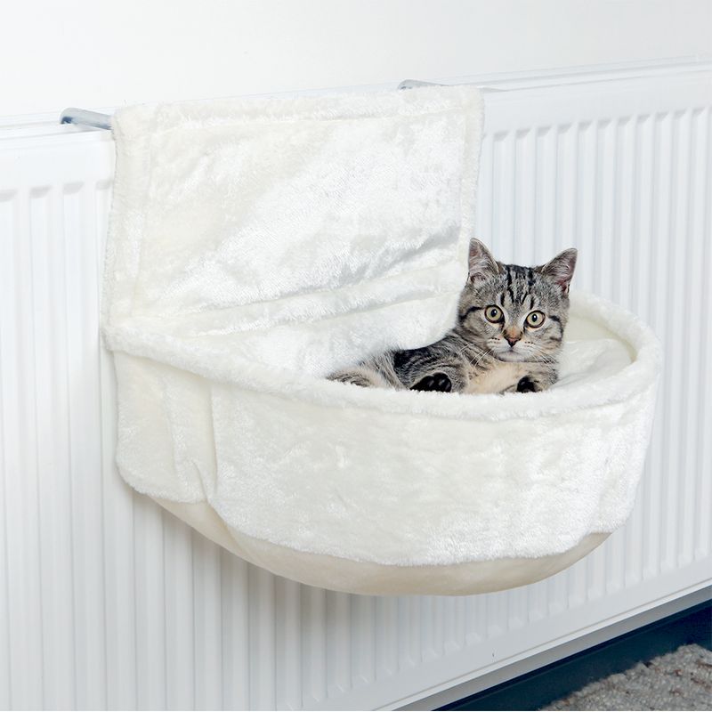 Cat bed made of white plush, attached to a radiator. Grey cat lying relaxed in the bed.