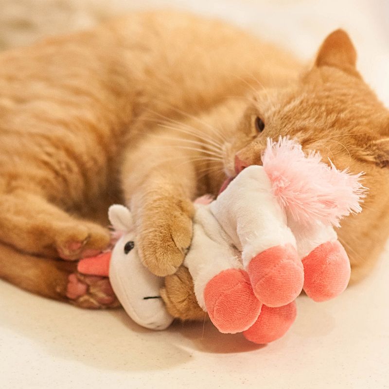 Red cat playing with a plush unicorn toy with pink and white details.