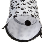 Toy tunnel made of white fabric with black paw patterns, grey material inside and a hanging black ball on a string.