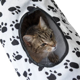 Cat tunnel made of white fabric with black paw patterns, cat looking through the opening.