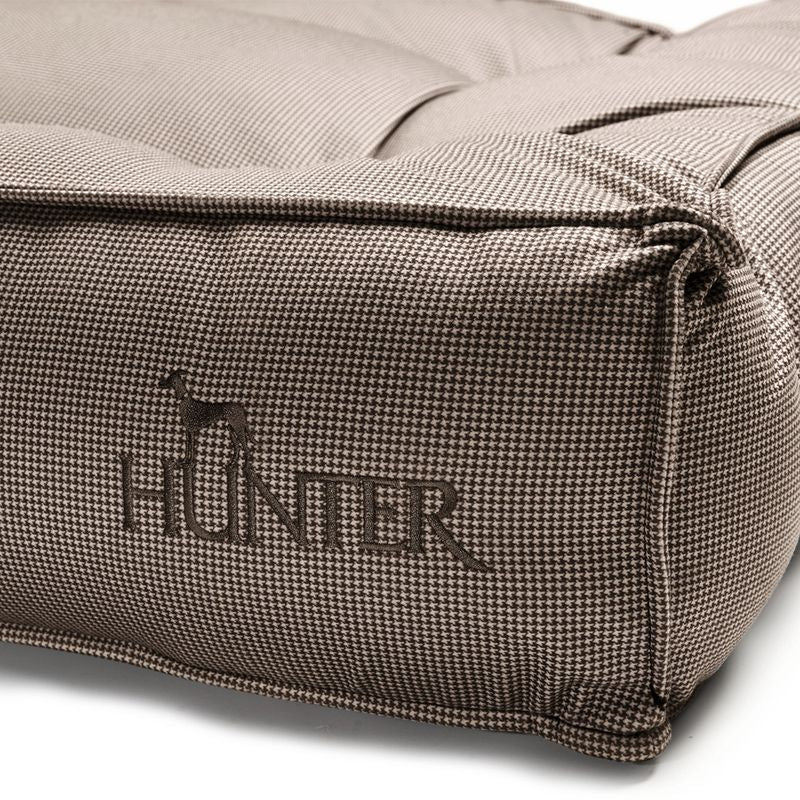 Close-up of a brown dog cushion with houndstooth pattern and embroidered 'Hunter' logo with dog silhouette.
