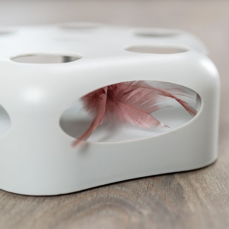 White toy with oval openings showing a pink feather. Suitable for interactive play.