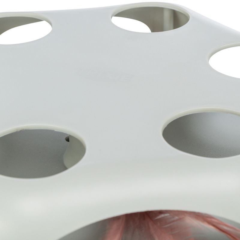 White plastic toy with round openings and a red feather inside, visible through the holes.