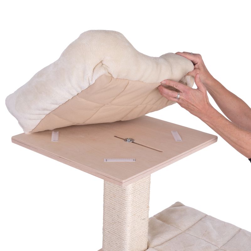 Demonstration of the removable cushion on a wooden platform of a scratching post. Cushion is lifted by hands, Velcro fastenings for attachment are visible.