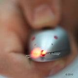Silver toy mouse with glowing red LED nose and fine wire whiskers, held in a hand.