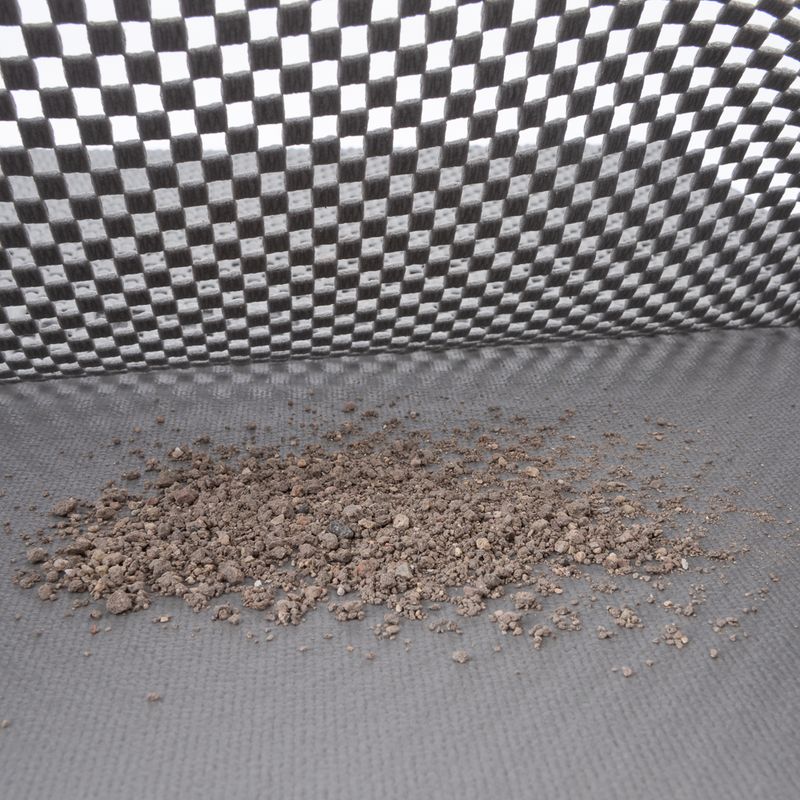 Close-up of cat litter on a grey, textured surface with a chequered background.