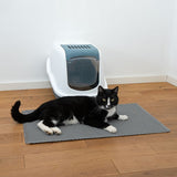 Closed cat litter box with grey mat in front, with a black and white tomcat lying on it. Shows use of the mat for cleanliness around the litter box.