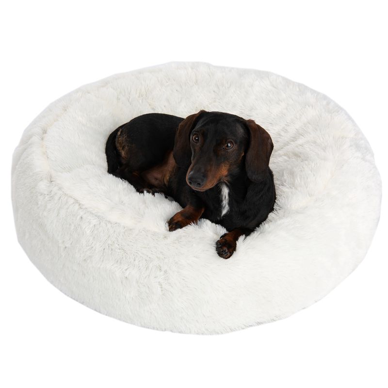 Dog lying on a white, fluffy pet bed. Round design with soft surface.