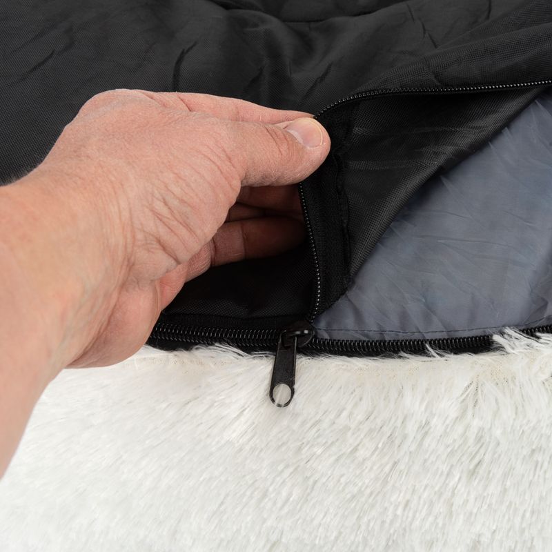Close-up of a zip on a black fabric cover with white faux fur. A hand opens the zip to reveal the inner material.