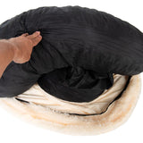 Hand lifting the black cover of a round, plush pet bed to show removable or washable inner padding.