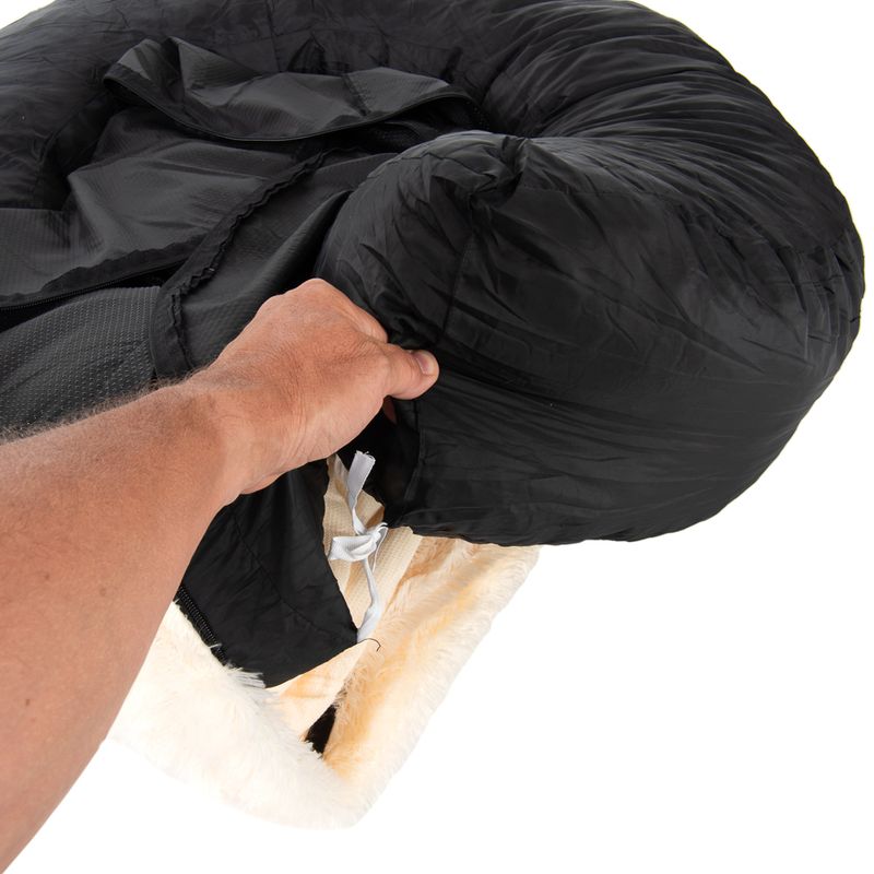 Hand demonstrating how to remove or adjust the black cover from a round, padded pet bed with a drawstring fastening.