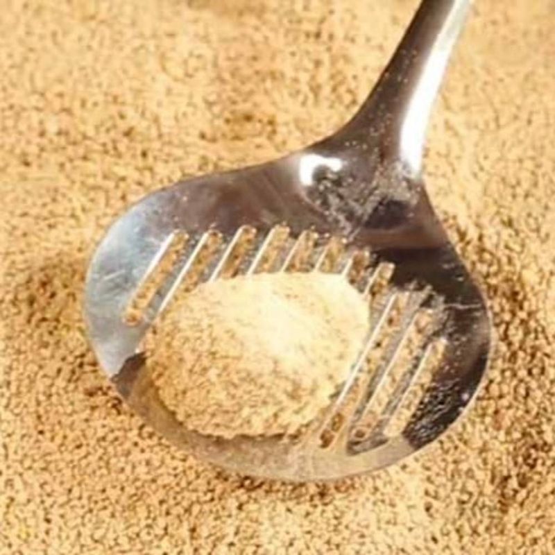 Clumping litter being scooped with a metal slotted scoop, showing how the litter forms solid clumps for easy removal.