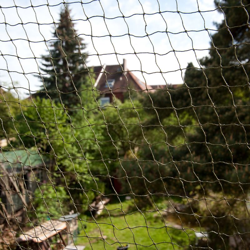 Protective net for outdoor areas, fine-meshed, transparent, with view of garden landscape in the background.