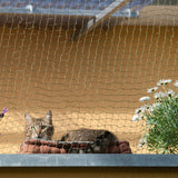 Cat safety net installed on balcony, protects cat from falling. Net with fine mesh structure, flowers and cat visible.