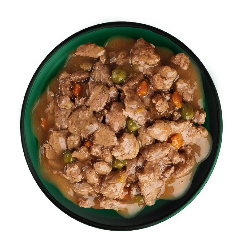 Chunks of meat with peas and carrots in gravy served in a bowl, showing the texture and ingredients of the wet pet food.