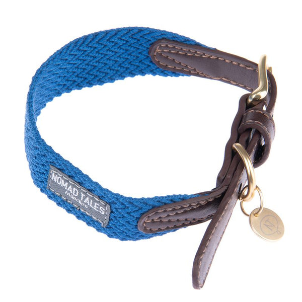 Nomad Tales dog collar made of blue fabric with brown leather accents, gold buckle and pendant.