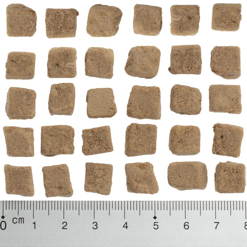 Brown, square food pieces approximately 1-2 cm in size, shown next to a ruler for size reference.