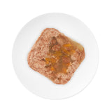 Close-up of wet food with meat pieces and vegetables on a white plate.