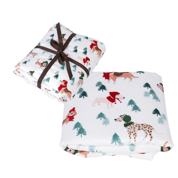 White blanket with dog motifs in winter clothing and green fir trees, folded and tied with a brown ribbon.