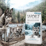 Wolf of Wilderness Junior Blue River. Grain-free recipe with free-range chicken, salmon, forest berries, roots and herbs. Packaging in front of river landscape.